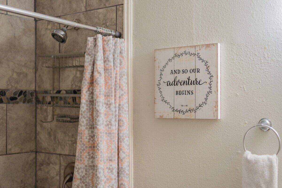 A bathroom with a shower, a floral curtain, and a sign on the wall.