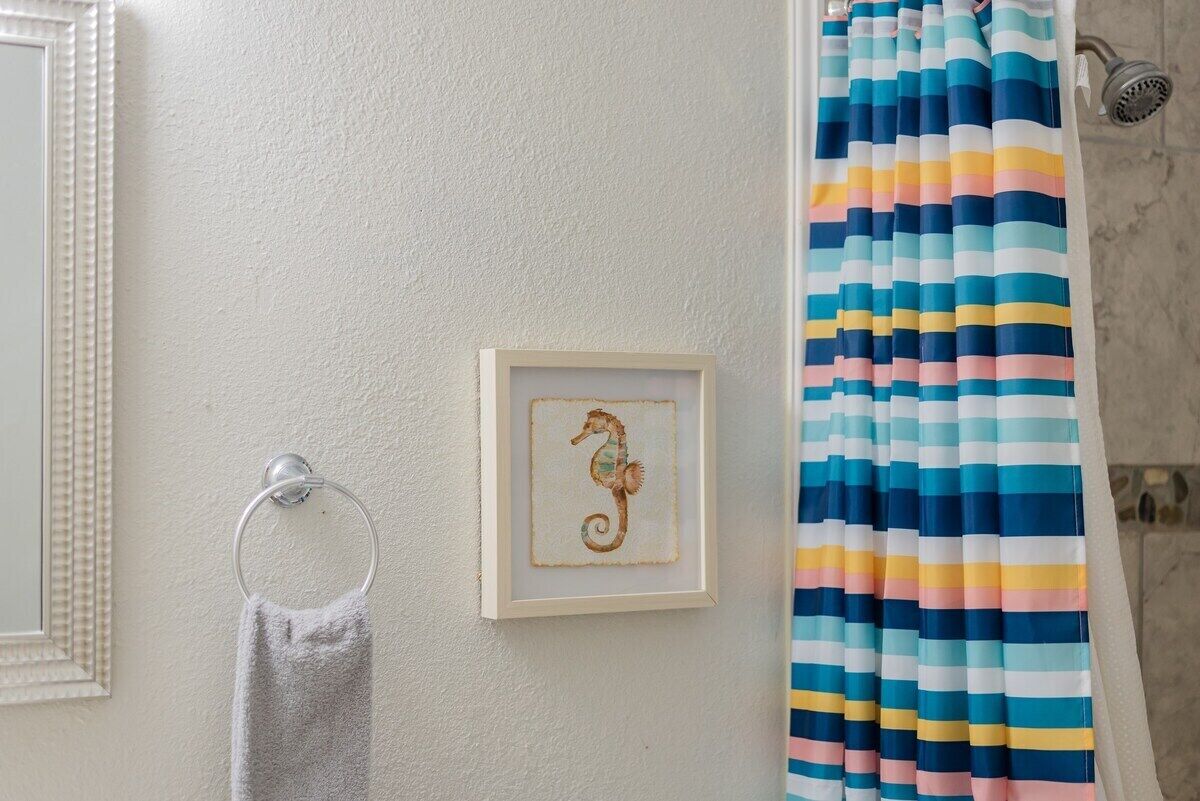 Un baño con cortina de ducha a rayas, una obra de arte con un caballito de mar enmarcado y un perchero para toallas.
