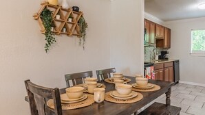 Una mesa de comedor dispuesta con cuencos, tazas y una jarrón, rodeada de sillas de madera.