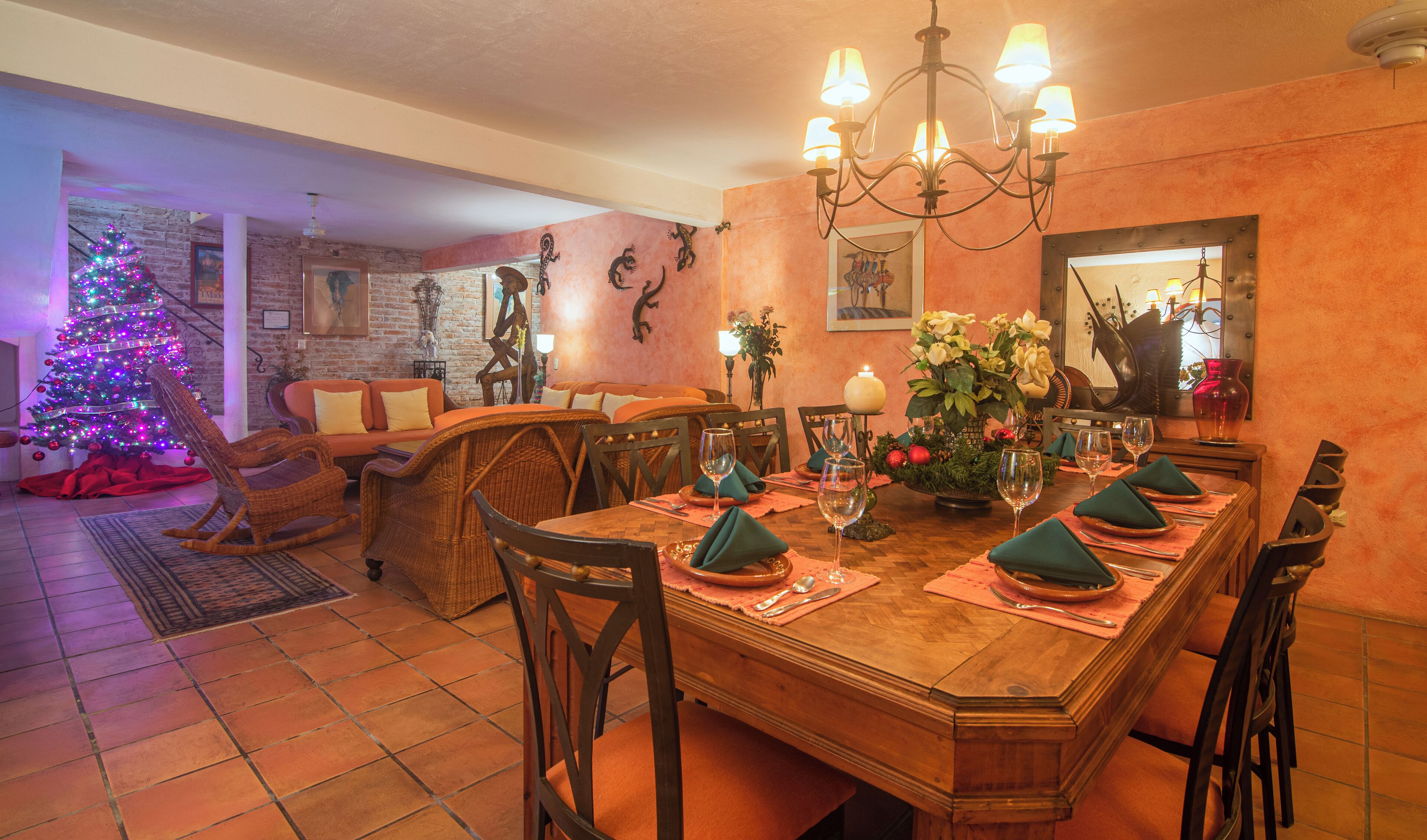 Un comedor con una mesa de madera dispuesta para seis personas, rodeada de sillas. Se ve un árbol de Navidad con luces de colores al fondo.