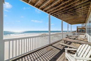 A wooden deck with white railings overlooking a beach.