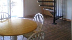 A room with a wooden ceiling, a spiral staircase, a round wooden table with chairs, and a sliding glass door leading outside. - Pine Cottage at Shiloh Cottages - Fenelon Falls (Fenelon Falls)