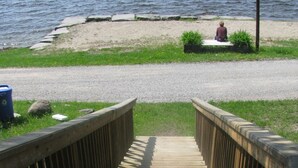 A wooden boardwalk leading to a sandy beach with a person sitting on the sand. - Pine Cottage at Shiloh Cottages - Fenelon Falls (Fenelon Falls)