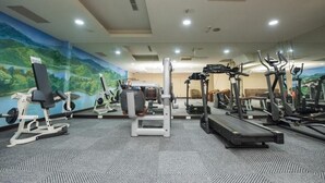 Un gimnasio con diverso equipo de ejercicio, incluyendo cintas de correr y máquinas de pesas, y un mural con un paisaje en la pared.