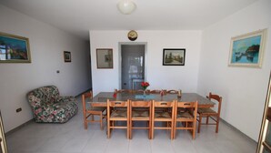 Ein Essbereich mit einem rechteckigen Tisch, sechs Stühlen, einer floralen Couch und einer Tür zu einem anderen Raum.