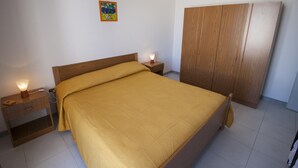 Ein Schlafzimmer mit einem Bett, einem Holzschrank, Nachttischen und einer Wandlampe.