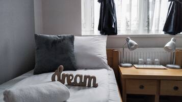 En snyggt bäddad säng med en kudde, en handduk och en träskylt med texten ”dröm”. Bredvid sängen står ett litet bord med en lampa och ett par glasögon.