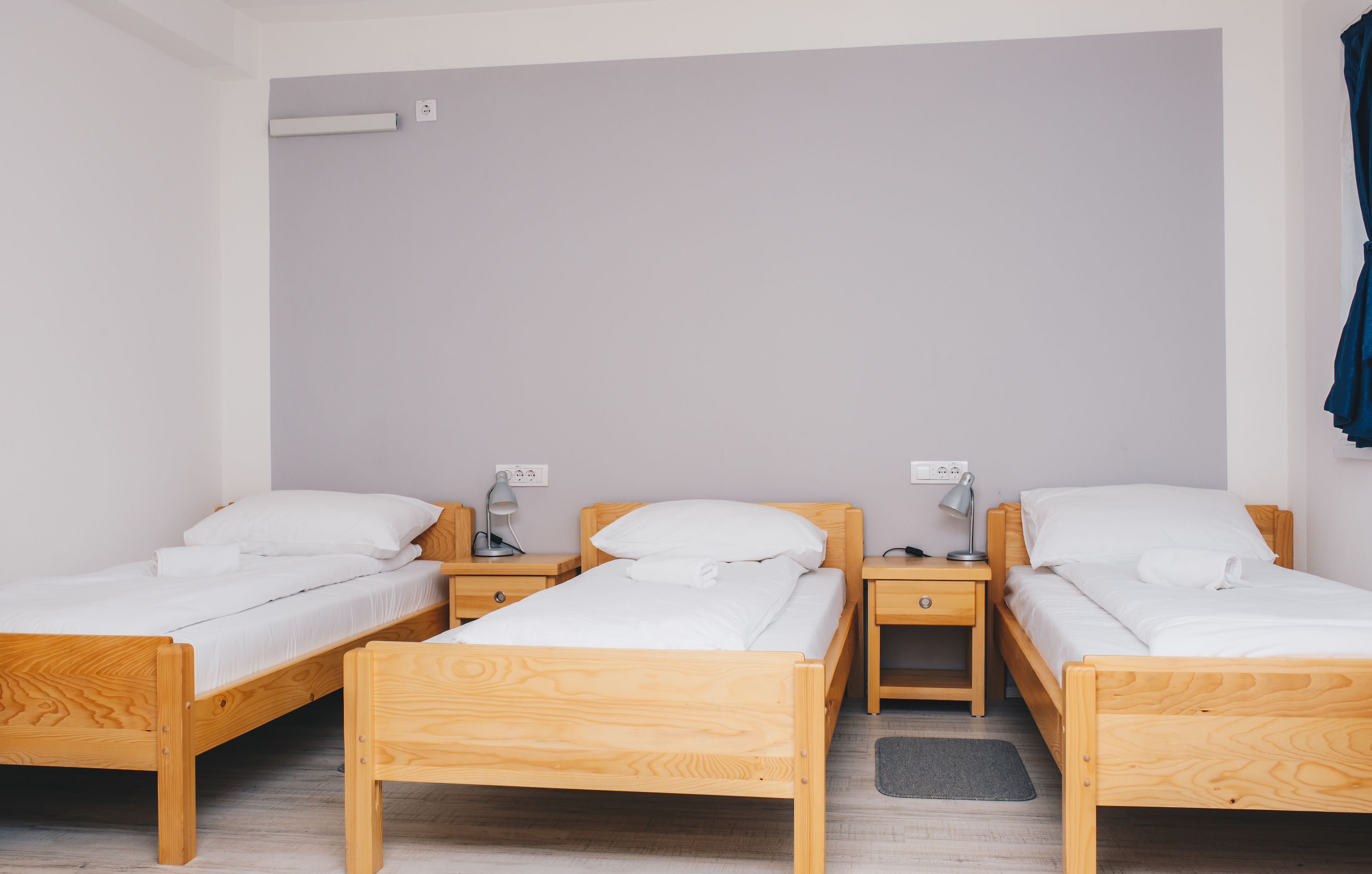 A room with three wooden beds, each with white bedding and a small bedside table with a lamp.