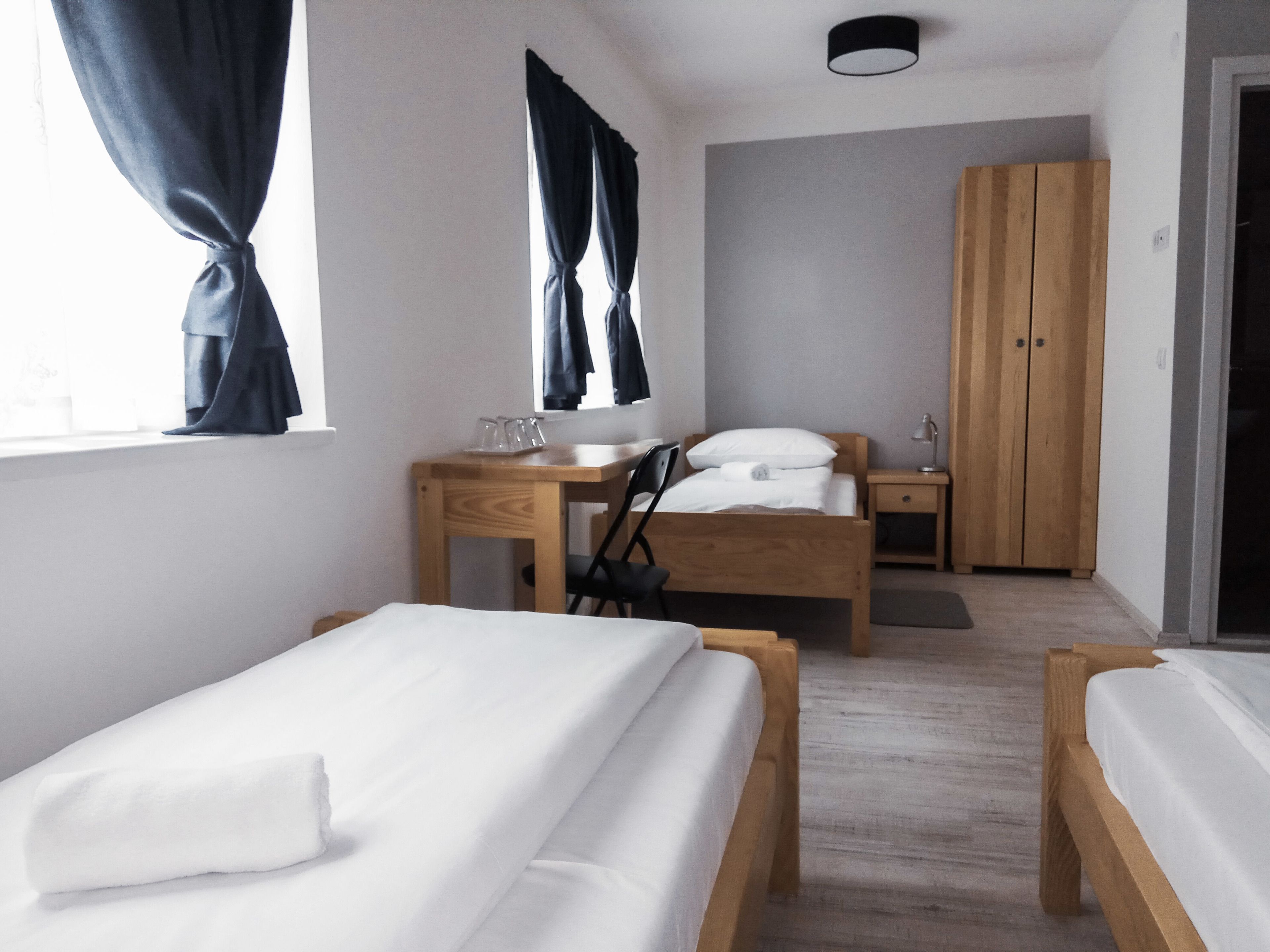 Una camera da letto con due letti singoli, una scrivania in legno con una sedia, un armadio e un comodino con una lampada.