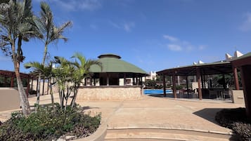 Zona de resort con piscina, zonas de estar cubiertas y palmeras.