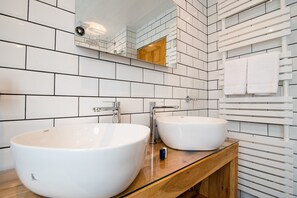 A modern bathroom with two white sinks, a wooden vanity, and a mirror above the sinks.