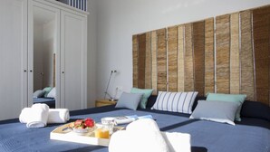 A neatly made bed with a tray of breakfast, towels, and a headboard with a woven pattern. - Singular Stays El Faro (Puçol)