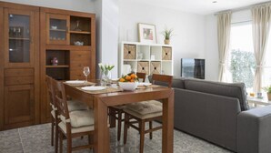 A dining area with a wooden table and chairs, a grey sofa, and a TV on a stand. - Singular Stays El Faro (Puçol)