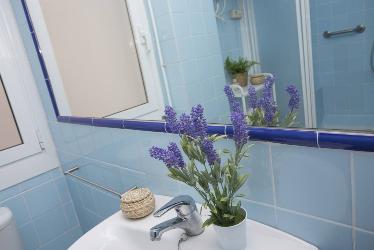 Une salle de bain avec des carreaux bleus, un lavabo blanc, un robinet argenté, un pot de lavande et un panier en osier.