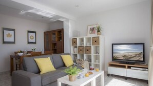 A modern living room with a grey sofa, a white coffee table, a TV on a stand, and a bookshelf. - Singular Stays El Faro (Puçol)