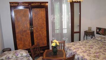Una stanza con due letti, un tavolo di legno con un vaso di fiori, una sedia, un armadio in legno, uno specchio e un lampadario.