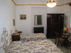 A bedroom with two beds, a dresser, a mirror, a chandelier, and a small table with flowers. - Guest House Al Gattopardo (Favignana)