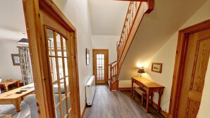 Un escalier en bois menant au deuxième étage, un couloir avec un radiateur et un coin repas avec une table et des chaises.