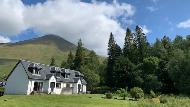 Une maison avec un toit en pente, un porche à l’avant et une pelouse bien entretenue.