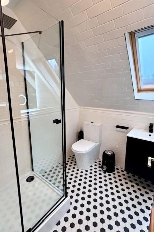Een badkamer met een douchecabine van glas, een wit toilet, een zwarte koffiezetapparaat en een zwarte wastafel.