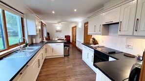 A modern kitchen with white cabinetry, a black countertop, and a wooden floor. - 4 star, 4 bedroom, 3 bathroom Scottish cottage with stunning loch and mountain views (Crianlarich)