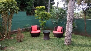A small outdoor seating area with wicker chairs and a round table, surrounded by greenery and a green wall. - Enrich Bungalow (Kandy)