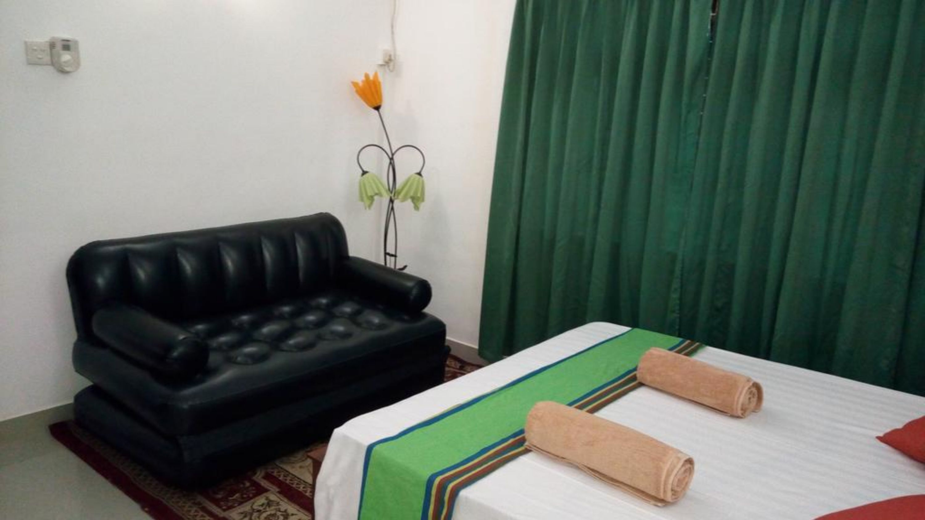 A room with a black sofa, a bed with a green and white striped bedspread, and a green curtain.