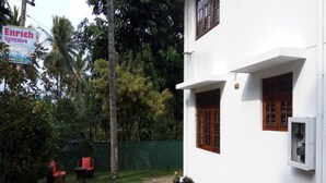 A white building with a paved courtyard, a green fence, and a sign for an Enrich Bungalow. - Enrich Bungalow (Kandy)