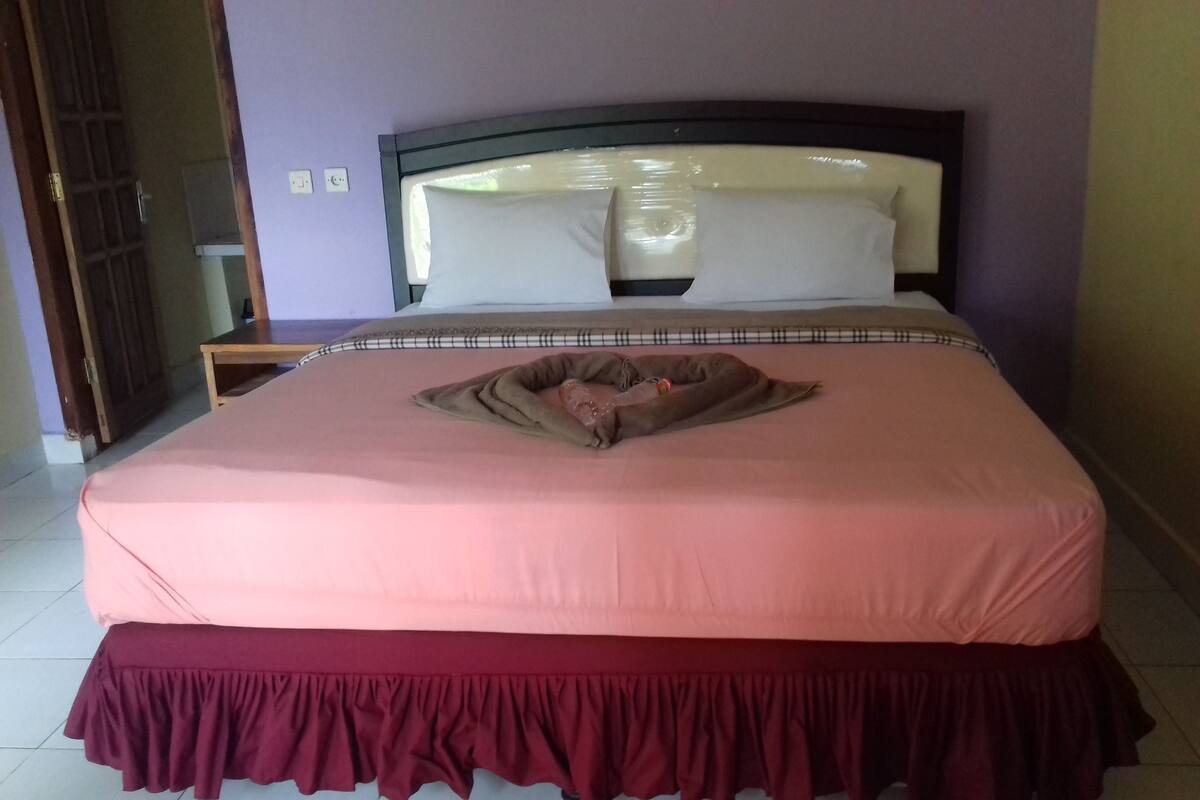 A bed with a pink bedspread and a maroon skirt.