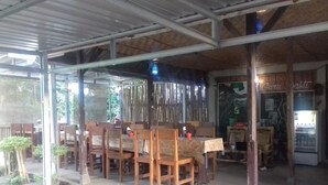 Un espace extérieur aménagé pour les repas, avec des tables et des chaises en bois, un coin salon abrité et une devanture de magasin bien visible avec une enseigne.