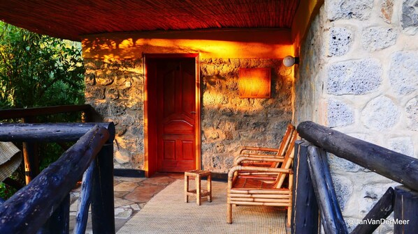 Step into this charming building with a rustic wooden door and a cozy porch area featuring a chair and table.