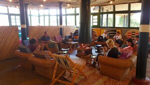 Eine gemütliche Lounge-Ecke mit Korbmöbeln, einem zentralen Feuerkorb und großen Fenstern, die viel Tageslicht hereinlassen.