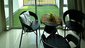 A balcony with a view of a green lawn and houses, furnished with two chairs and a small table with a vase of sunflowers. - Lux Desaru Villa (Bandar Penawar)