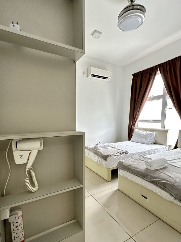 A hotel room with a bed, a bedside table, a telephone, an air conditioning unit, and a window with curtains.