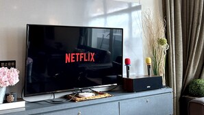 A modern living room with a flat-screen TV displaying the Netflix logo, a grey entertainment unit, and a window with curtains. - Lux Desaru Villa (Bandar Penawar)