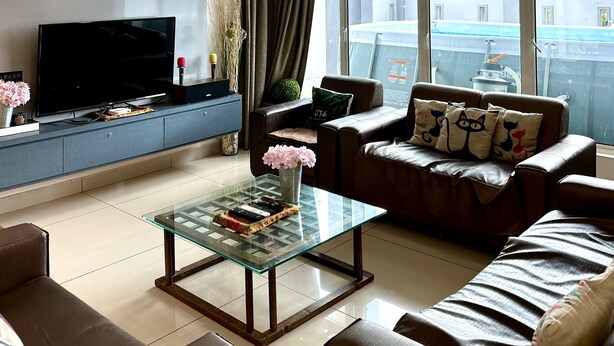 A modern living room with a flat-screen TV, leather sofas, a glass coffee table, and large windows offering a view of the city. - Lux Desaru Villa (Bandar Penawar)