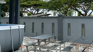 A rooftop terrace with a pool, seating area, and a view of surrounding buildings and trees. - Lux Desaru Villa (Bandar Penawar)