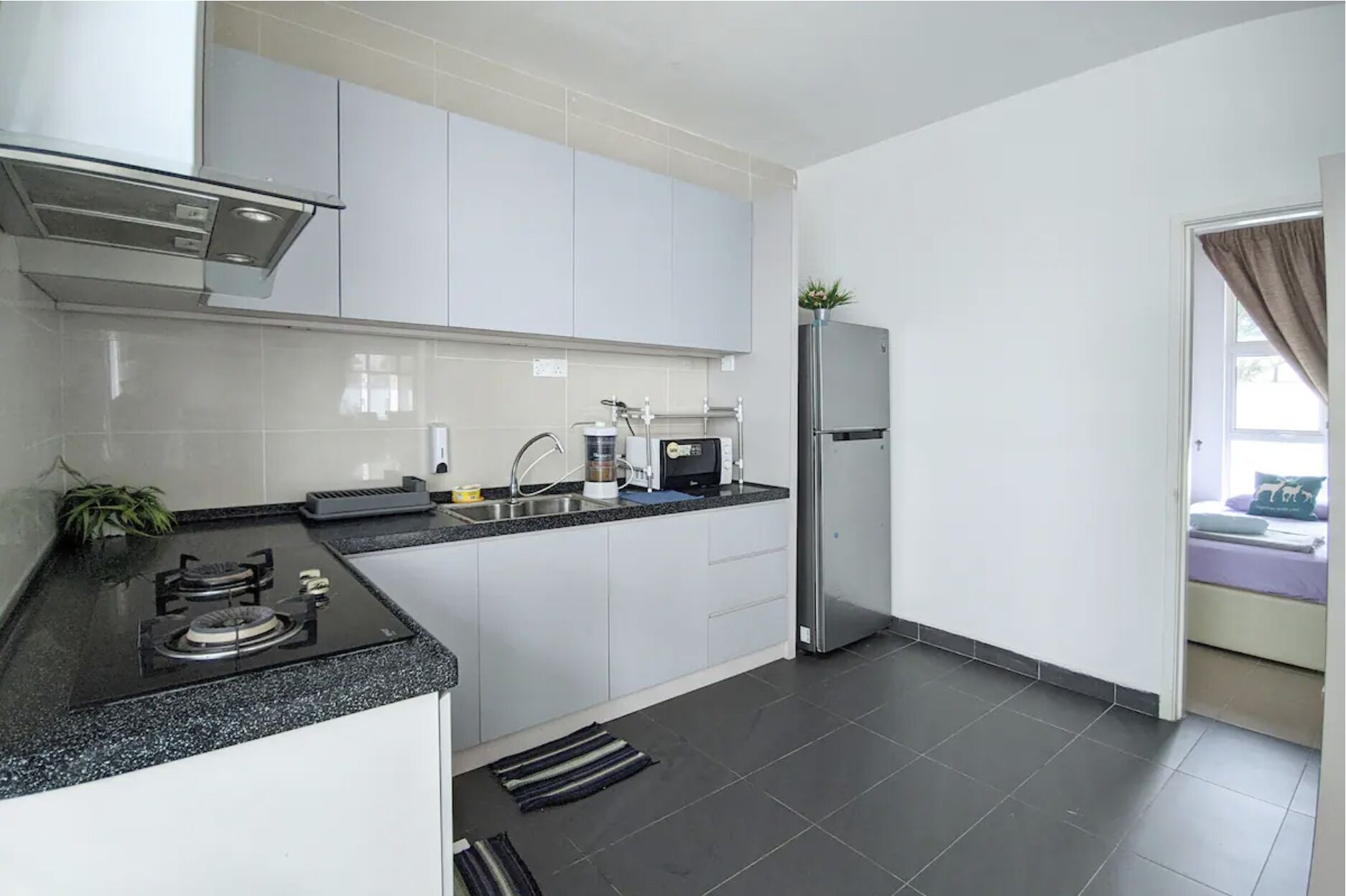 Una cocina moderna con armarios blancos, encimera negra, pileta de acero inoxidable, microondas y refrigerador.
