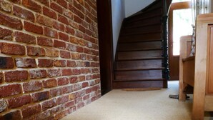 Quarto com parede de tijolos, escada de madeira e um par de sapatos em um piso tecido.