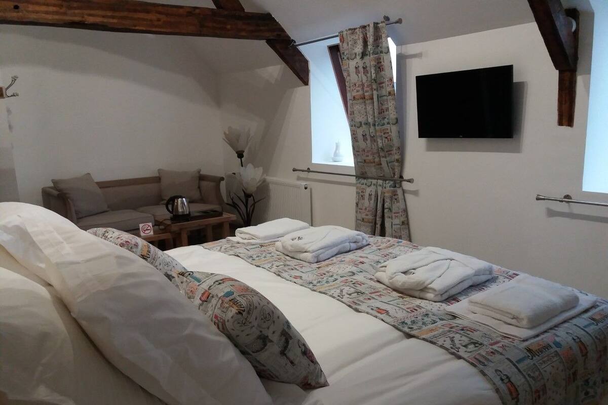 Um quarto com uma cama grande, uma televisão presa na parede e uma janela com cortinas.