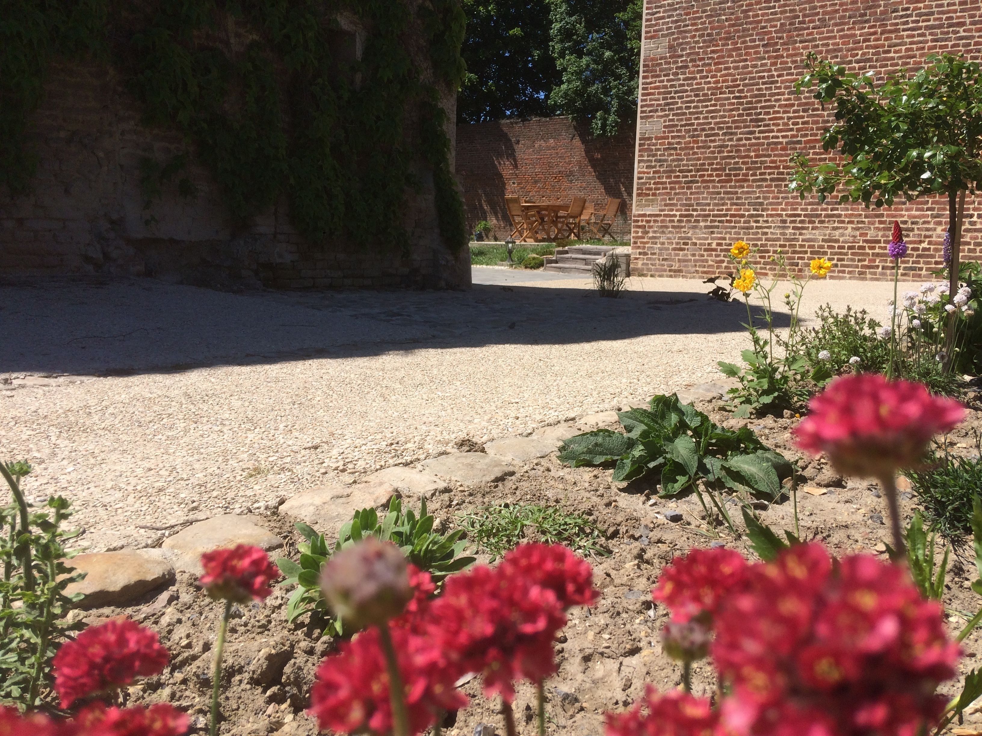 Ein Innenhof mit Kiesweg, einem Backsteinhaus und verschiedenen Pflanzen und Blumen.