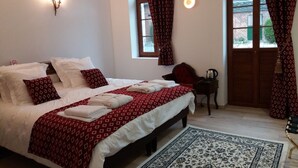 Quarto com cama grande, mesa pequena, cadeira e janela com cortinas.