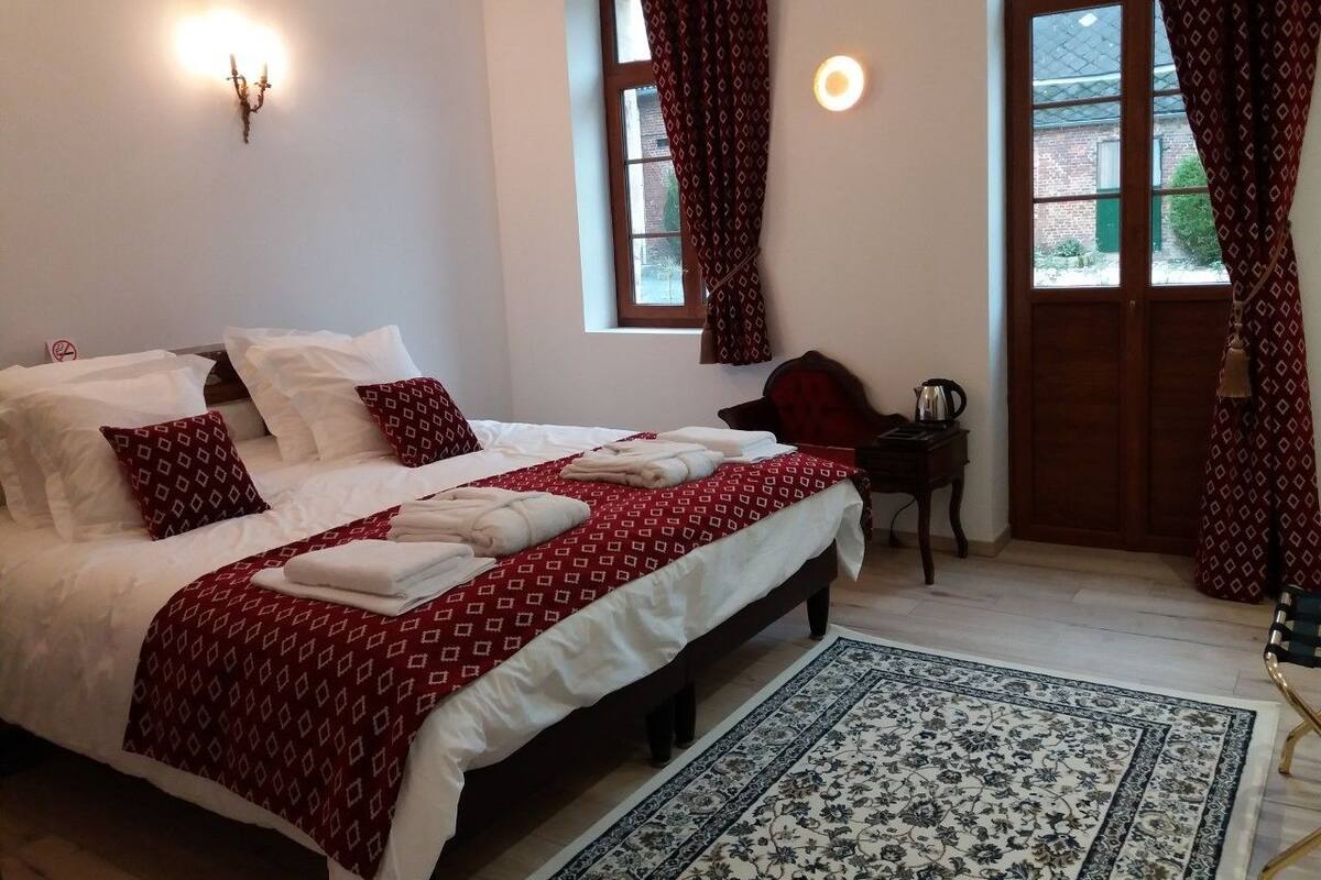 Quarto com cama grande, mesa pequena, cadeira e janela com cortinas.