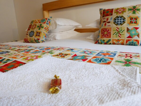 A bed with a colorful quilt, white pillows, and a white towel with a small item on it. - La Boussieroise (Boussières-en-Cambrésis)