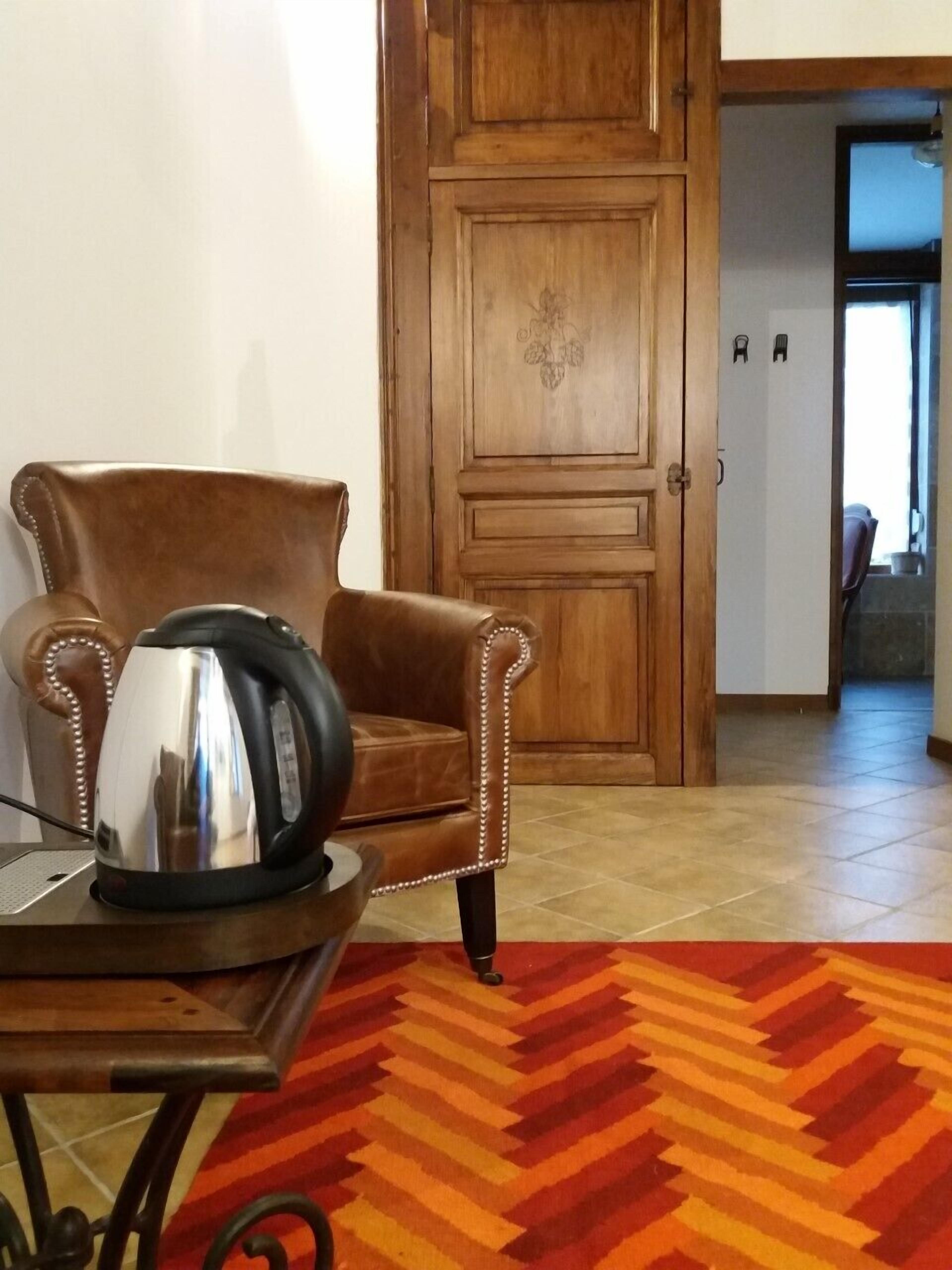 Una habitación con un sillón de cuero marrón, una mesa con un hervidor y una alfombra estampada.