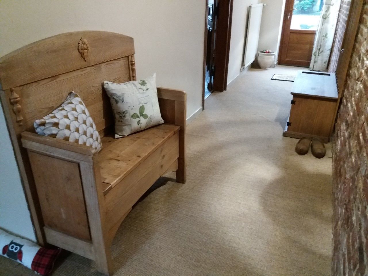 Un banco de madera con dos almohadones, una pequeña mesa de madera y un par de zapatos en el suelo.