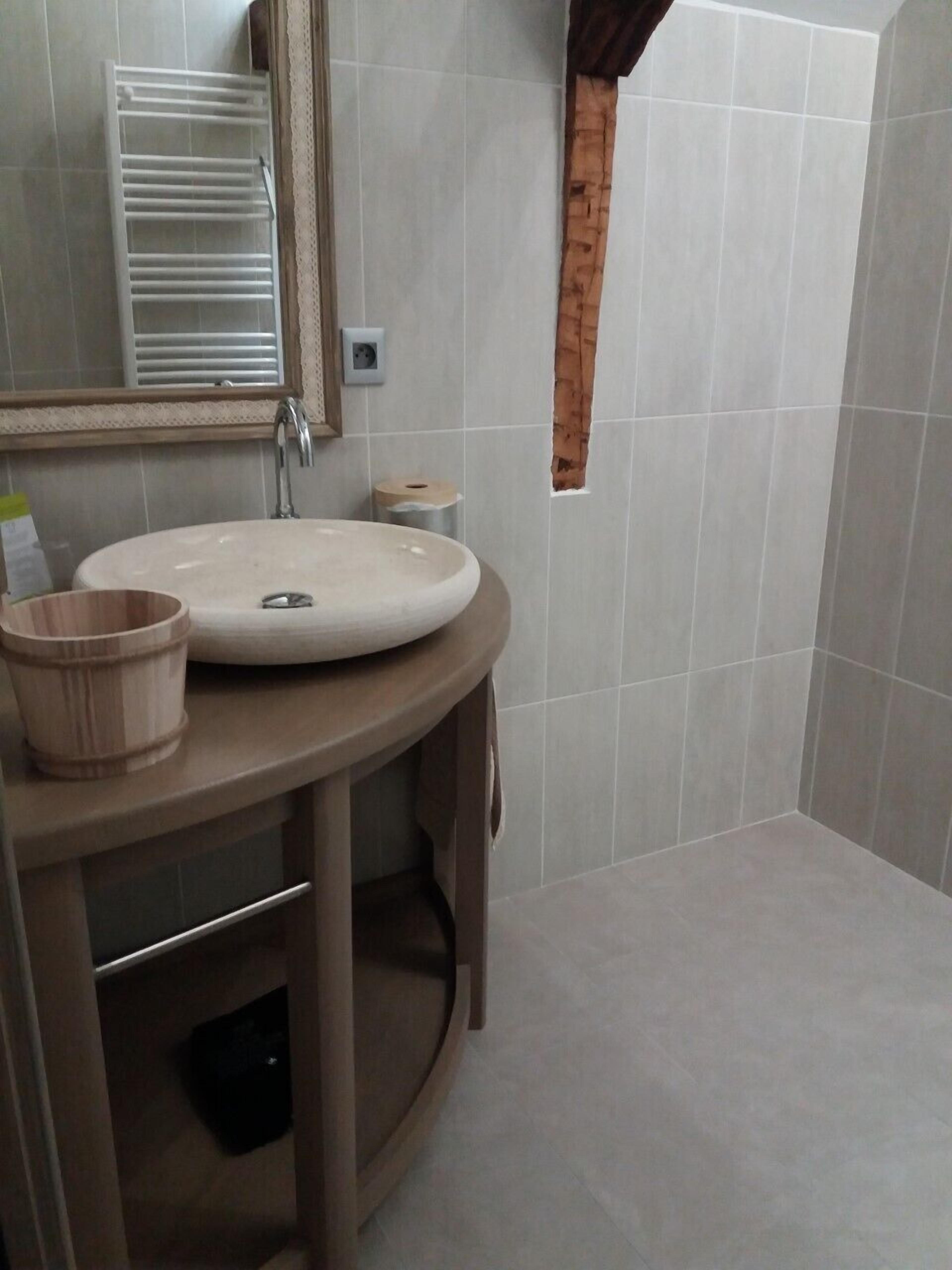 A bathroom with a round sink, a wooden cup holder, a towel rack, and a mirror.