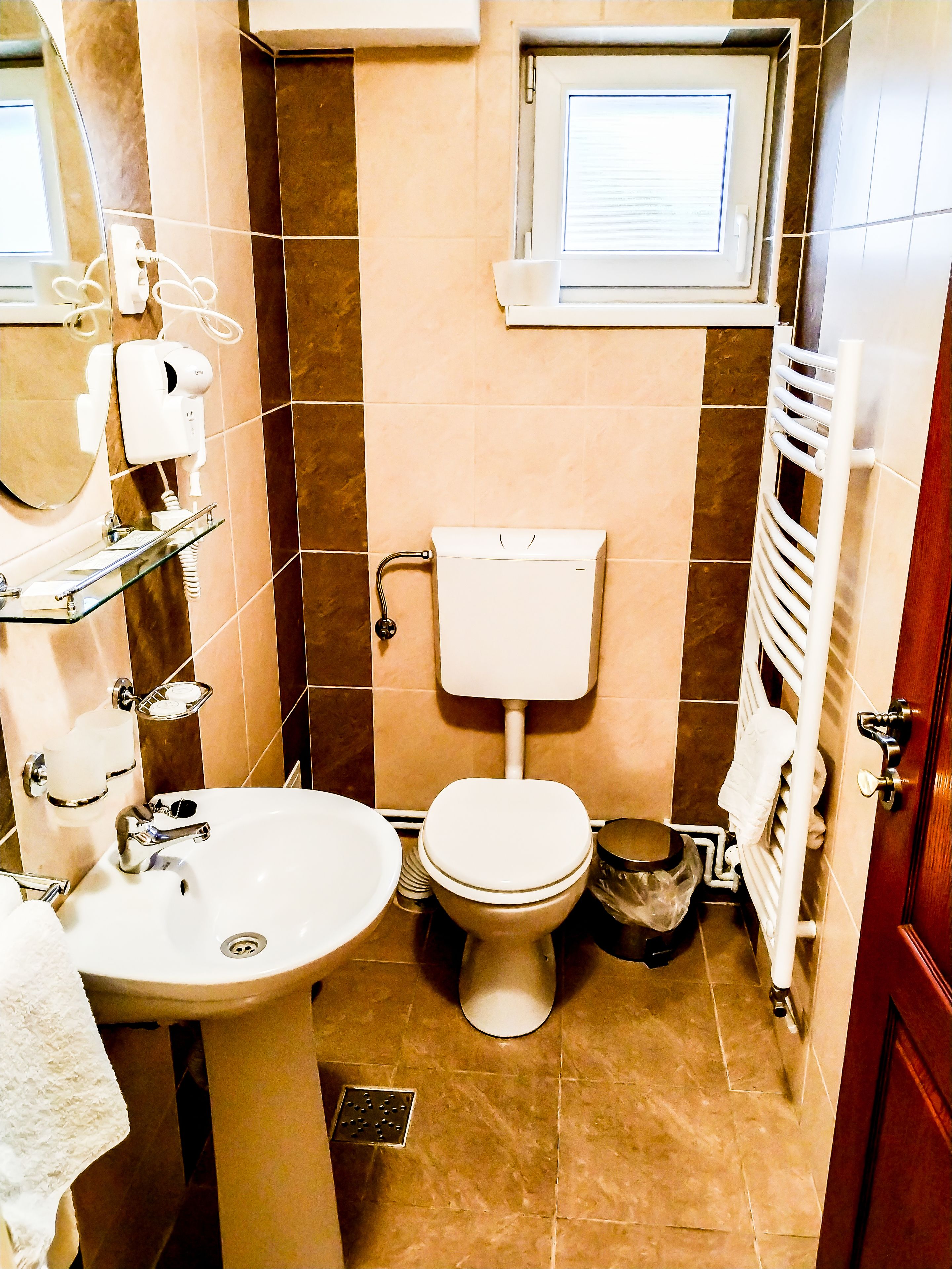 A bathroom with a toilet, sink, mirror, towel rack, and a window above the toilet.