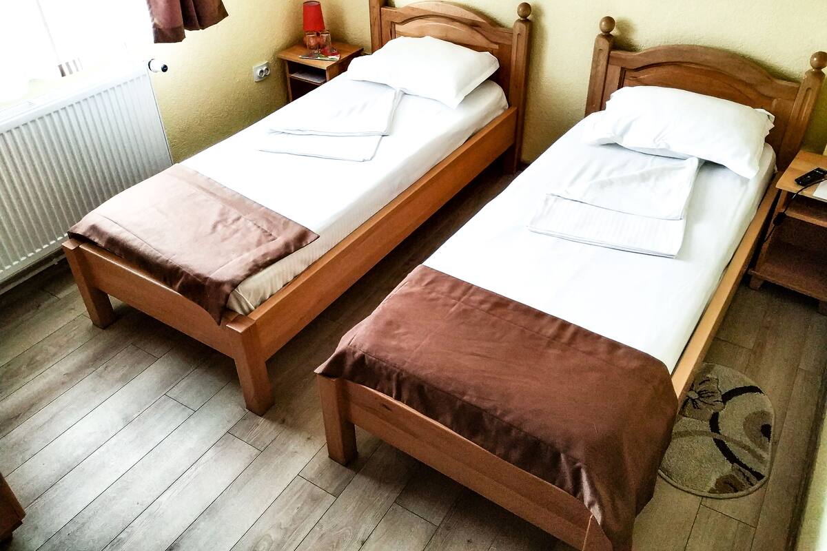 Duas camas de madeira com lençóis brancos e mantas marrons em um quarto com piso de madeira e um radiador.