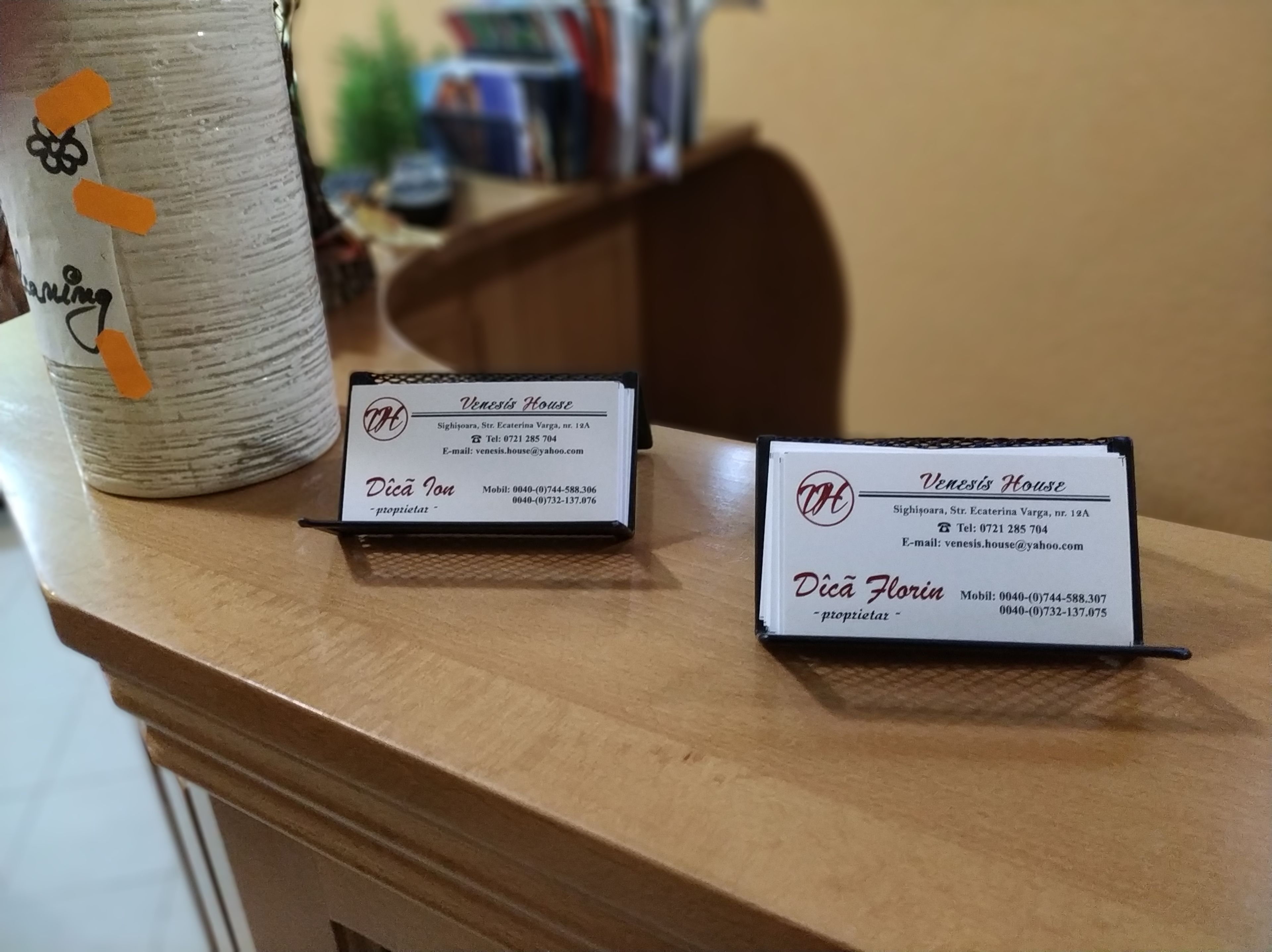 Dos tarjetas de presentación sobre una mesa de madera, una con la etiqueta 'Venesis House' y la otra con 'Dica Florin'.